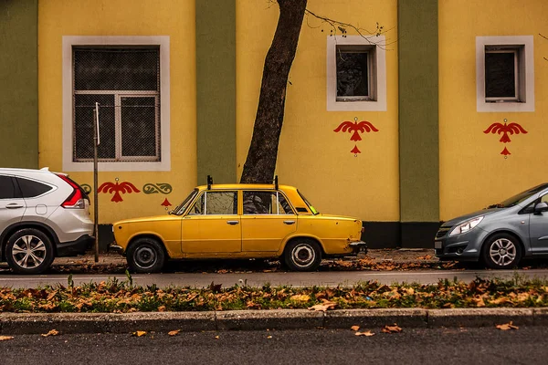 an old yellow Russian car parked between two new cars. the difference between different car manufacturers. the difference between the poor and the rich.