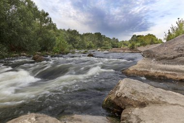 Kayalık sahilleri, rapids, hızlı Nehri akış, parlak yeşil bitki örtüsü ve bulutlu bir mavi gökyüzü yaz aylarında