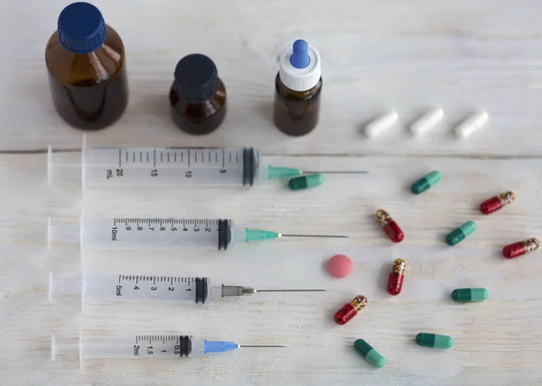 Spritzen und Kapseln, medizinische Ampullen und Tabletten auf einem weißen Holztisch. — Stockfoto