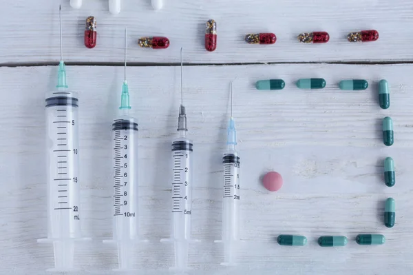 Seringues médicales, capsules, pilules reposent verticalement sur une table en bois peint en blanc grossièrement . — Photo