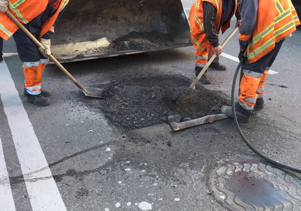 La brigada de trabajadores despeja una parte del asfalto con palas en la construcción de carreteras — Foto de Stock