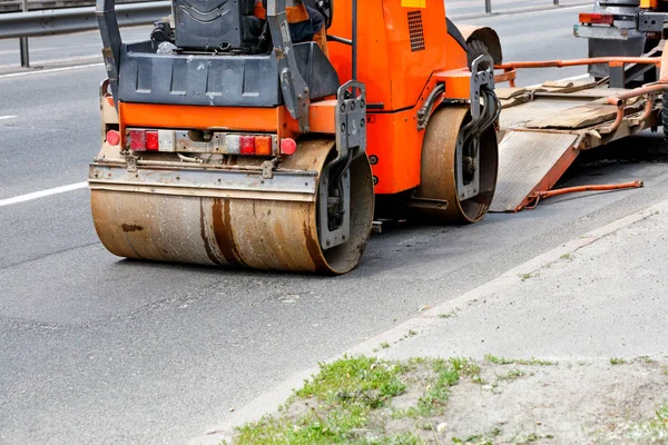 Heavy vibrating road roller is unloaded from a low platform trailer and drives onto the carriageway.