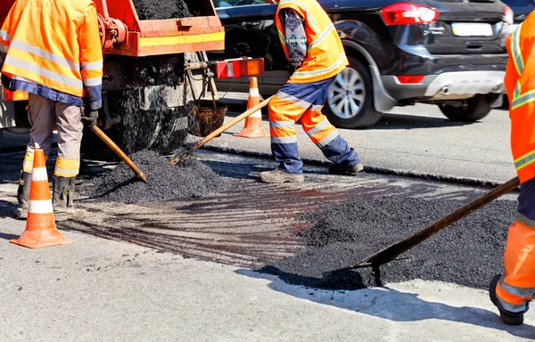 Equipo de trabajo nivela el asfalto fresco con palas en un área reparada en la construcción de carreteras . — Foto de Stock