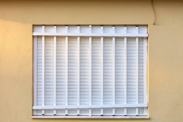 Witte metalen luiken op het raam van de gevel van het huis zijn afgesloten met een witte metalen rooster. — Stockfoto