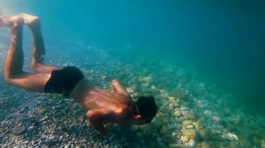 Sportif bir genç suyun altına dalıyor ve yüzme tarzıyla kameranın önünden geçiyor açık mavi tropikal sularda yavaş yavaş derinliklere iniyor, Gopro 7 siyah..