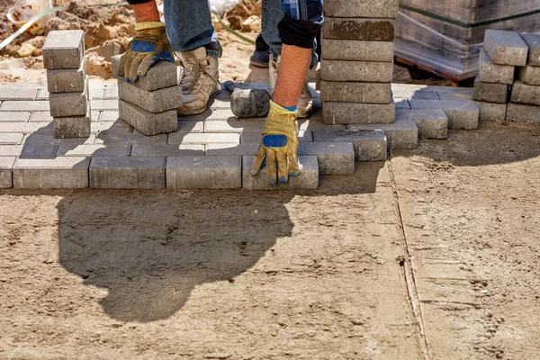 Un trabajador pone losas de pavimentación en una plataforma plana de arena preparada en la acera en un día soleado brillante . — Foto de Stock
