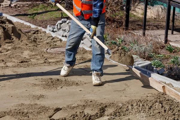 Elinde kürek olan bir işçi, döşeme levhalarının altındaki zemini yıkmak için kum giyer.. — Stok fotoğraf