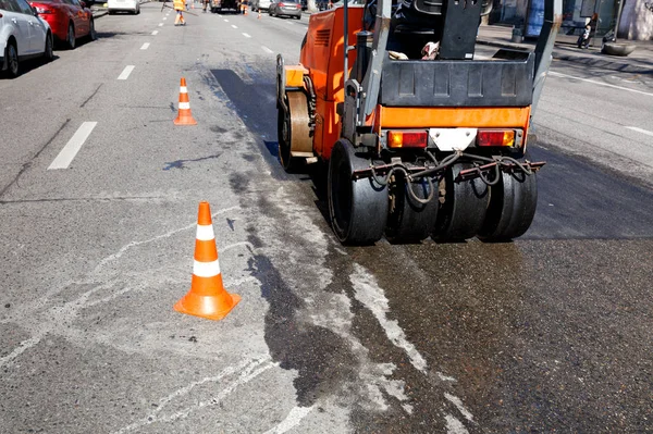 Rodillo de carretera vibratorio naranja pesado compacta asfalto en la parte reparada de la carretera de la ciudad . — Foto de Stock