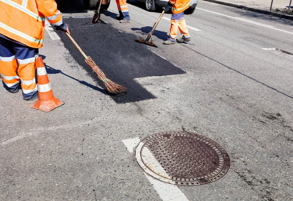 Al reparar la carretera, el equipo de trabajo vierte asfalto caliente en parches uniformes con palas, un nivel y una escoba manualmente . — Foto de Stock