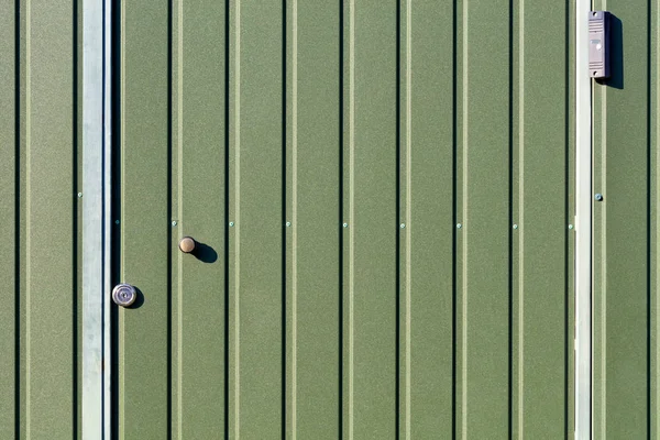 Groene metalen hek en deuren gemaakt van golfplaten met verticale rails en een bewakingscamera. — Stockfoto