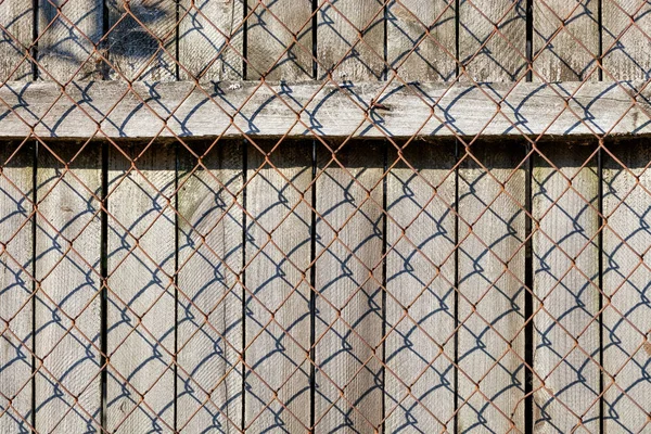 Zvětralý starý šedý plot je uzavřen zrezivělou síťovinou. — Stock fotografie