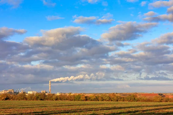 Wiejski jesienny krajobraz, jasne poranne słońce oświetlają pole uprawne, kompleks produkcyjny na horyzoncie i wysokie zachmurzone niebo. — Zdjęcie stockowe