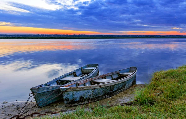 Dos viejos barcos azul-verdes amarrados por una cadena de metal a la orilla de un río tranquilo en el contexto del sol naciente brillante . — Foto de Stock