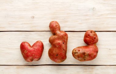 Çirkin, komik sebzeler, kalp şeklinde patatesler ve beyaz ahşap arka planda harf şeklinde. Pis sebzeler ya da yiyecek atıkları kavramı. Üst görünüm, alanı kopyala.