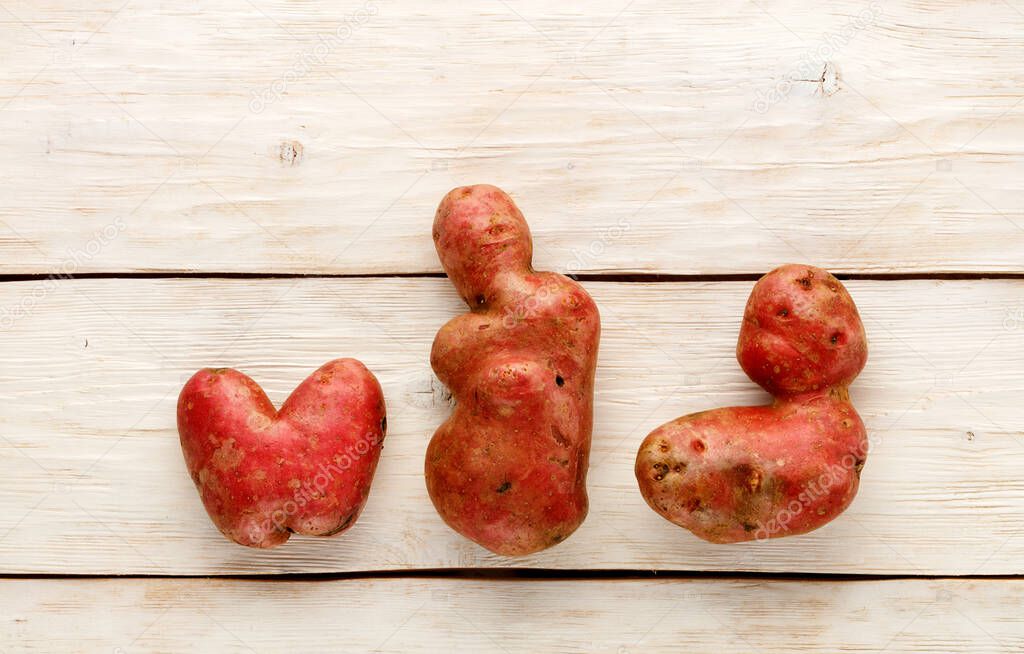 Ugly funny vegetables, heart-shaped potatoes and letter shape on a white wooden background. The concept of grungy vegetables or food waste. Top view, copy space.