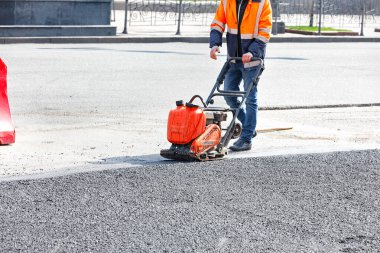 İşçi yol servisi, yol onarım alanında asfaltı sıkıştıran titreşimli plaka sıkıştırıcı kullanıyor.