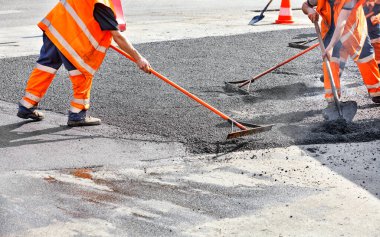 The road workers' working group updates part of the road with fresh hot asphalt and smoothes it for repair with a metal levels and shovels. clipart