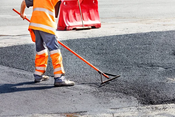 一名道路服务人员用新鲜的热沥青对一段道路进行了更新 并用金属平整 以进行人工维修 — 图库照片