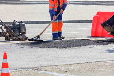 Yol yapımcısı, yeni asfaltı titreşen bir plakanın arka planına ve yol buldozerinin bir parçasına karşı ahşap bir seviyeyle düzleştiriyor..