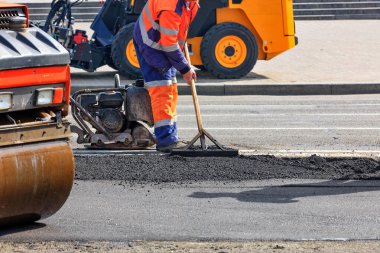 Bir yol işçisi yolun bir bölümünü paten pisti, rammer, buldozer ve ahşap katıyla onarıyor..