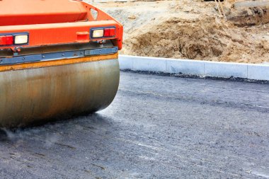 Büyük titreşim silindirinin metal silindiri, yol yüzeyindeki yeni asfaltı güçlü bir şekilde doldurur..