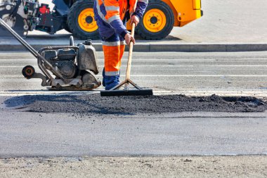 Bir yol işçisi yolun bir bölümünü paten pisti, rammer, buldozer ve ahşap katıyla onarıyor..