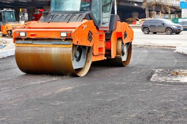 Ağır turuncu titreşimli buz pateni pisti, yeni bir yol kenti caddesi inşaatında sıcak asfaltı sıkıştırıyor..