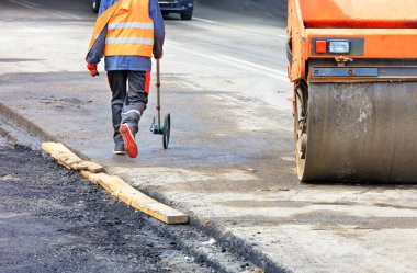 Ölçüm tekeriyle yol mesafesini ölçen bir mühendis büyük bir vibratörün yanında yürüyor..