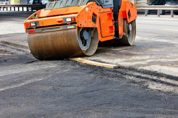 The metal cylinders of a large vibratory roller roll onto a new section of the road surface for powerful tamping of fresh asphalt.