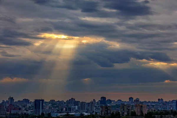 The sun's rays break through dense clouds at dawn over a sleeping city. Shining light in the dramatic morning sky.
