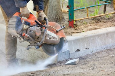 Beton kesici kullanan bir işçi açık bir alanda beton bir toz bulutunun içinde beton kaldırımları keser..