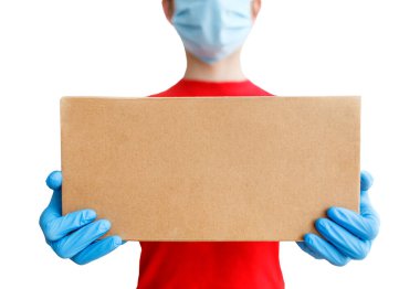 Elinde karton bir kutuyla kurye teslimat servisi. Tıbbi maskeli ve lastik eldivenli bir adam, kırmızı tişörtlü beyaz izole bir arka plan, sığ bir alan derinliği, seçici bir odak noktası var..