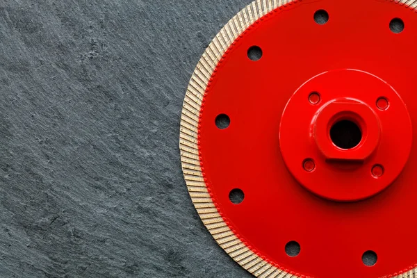 Cutting diamond professional blade of red color, a thin blade with a flange is used for precise cutting of the material against the background of gray granite, image with copy space.