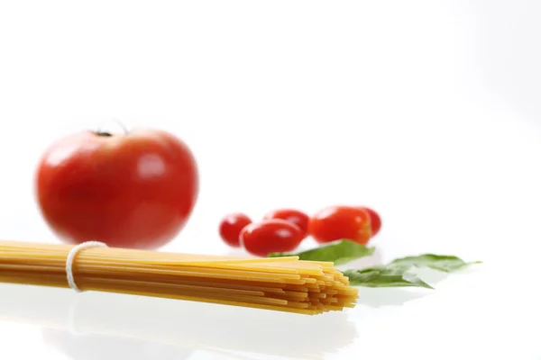 Fideos de espagueti crudos con tomates y albahaca aislados en blanco b — Foto de Stock