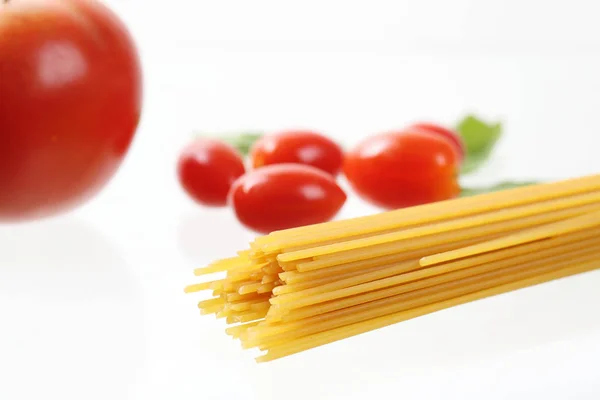 Fideos de espagueti crudos con tomates y albahaca aislados en blanco b — Foto de Stock