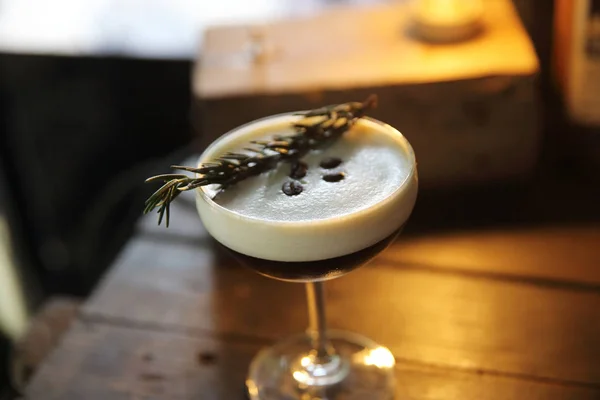 Coffee cocktail with coffee bean and rosemary on top with wood b