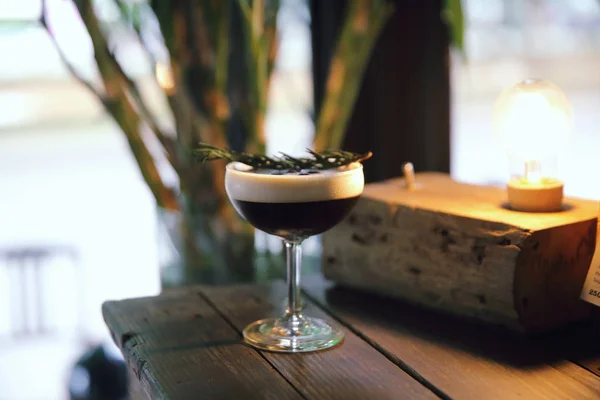 Coffee cocktail with coffee bean and rosemary on top with wood b