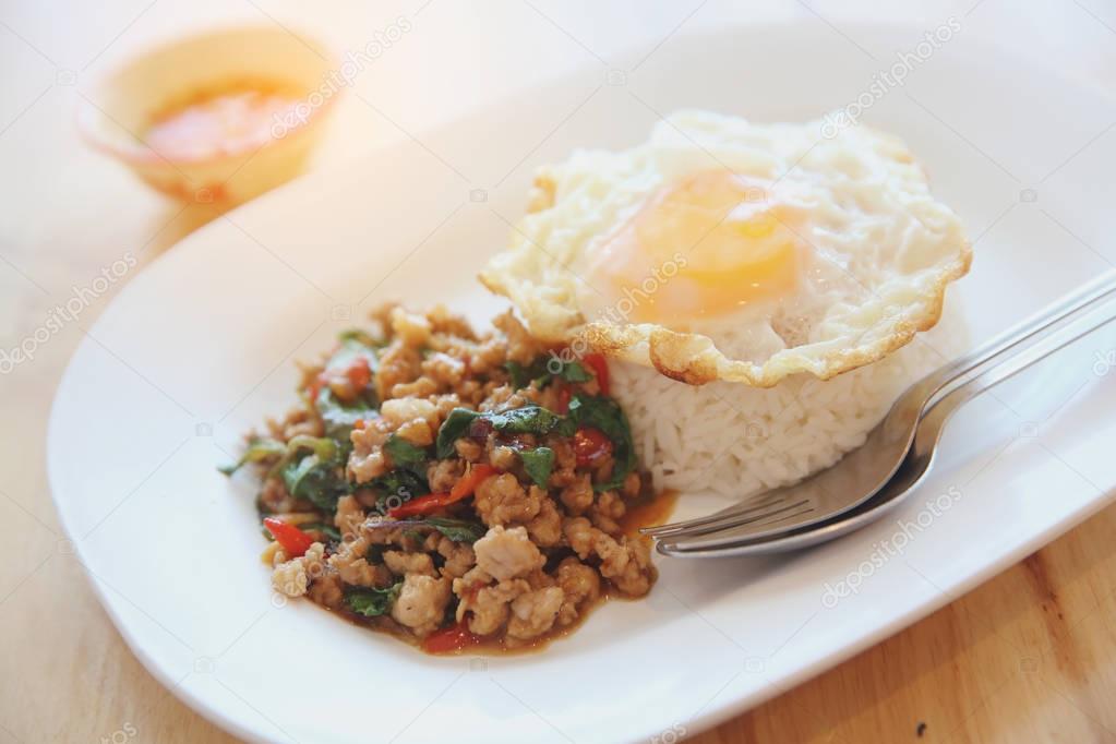 stir fried pork and basil with rice and egg on wood background t