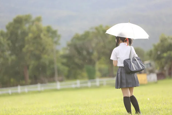 Escuela japonesa con sombrilla en la lluvia en el campo con hierba — Foto de Stock