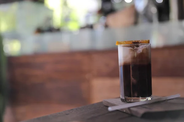 Ice black coffee with orange on wood background