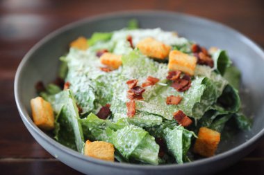 Kavrulmuş ekmek ve domuz pastırmalı Sezar salatası ahşap sırtına yakın.