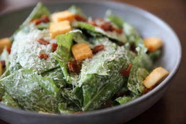 Kavrulmuş ekmek ve domuz pastırmalı Sezar salatası ahşap sırtına yakın.