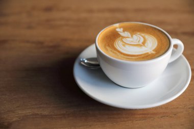 Kahve dükkanının ahşap masasındaki sütten yapılmış kapuçino ya da Latte sanat kahvesi.