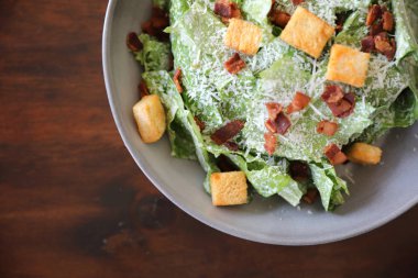 Kavrulmuş ekmek ve domuz pastırmalı Sezar salatası ahşap arka planda.