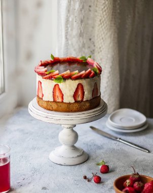 Masada bacağı olan bir tezgahta çilekli pasta. Hafif arkaplan, ev ortamı.