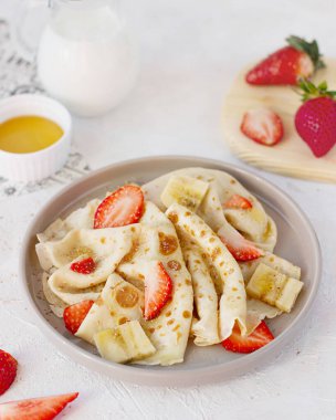 Çilekli bir tabak krep ve arka planda muz..