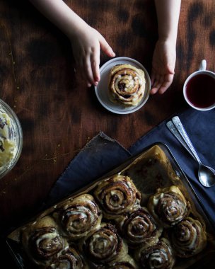 Kahverengi bir masada Cinnabon yuvarlıyor, çocuk kekini saklıyor, üst manzara..