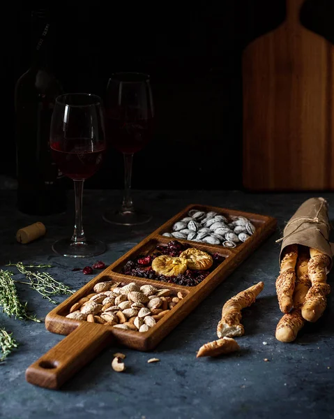 A long rectangular wooden mini-bar for snacks on a table with wine glasses.