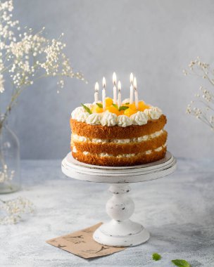 Beyaz kremalı sünger keki şeftali ve nane ile süslenmiş, üzerinde yanan mumlar var..