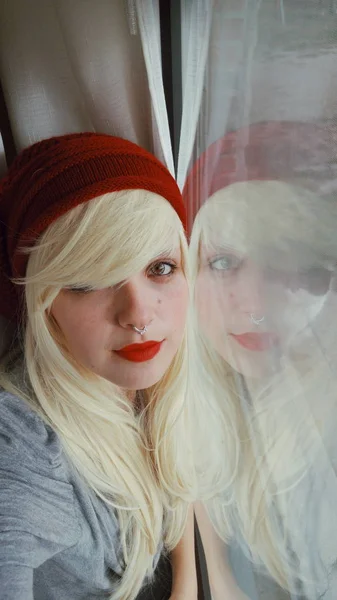 赤い唇と窓の近くのセーターに帽子と若いブロンドの女性の肖像画 — ストック写真